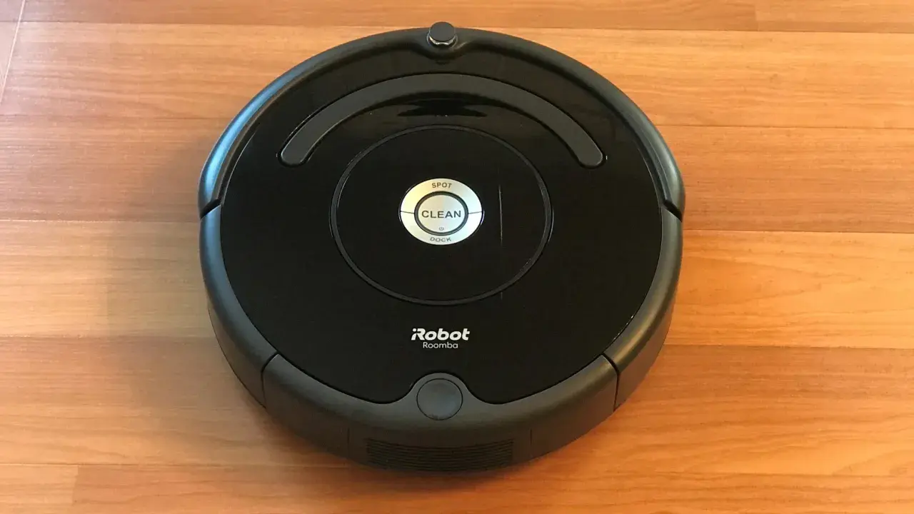 Un robot aspirador Roomba, uno de los modelos antiguos, descansa sobre un suelo de madera.