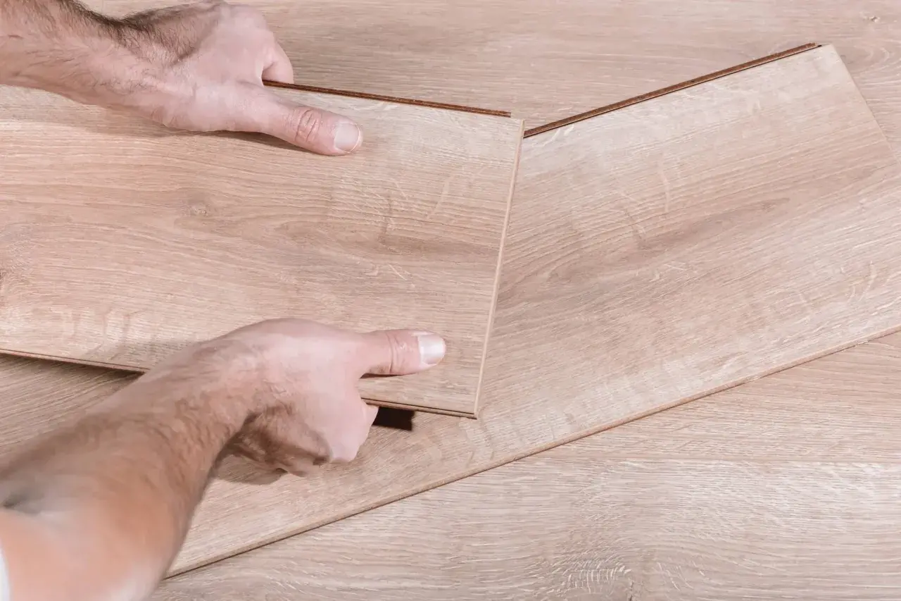 Manos desmontando una tabla de suelo laminado.