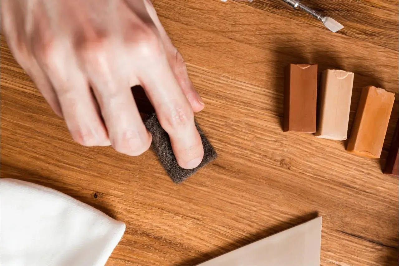 Mano lijando para reparar suelo laminado. Cera de colores y espátula listas para el retoque.