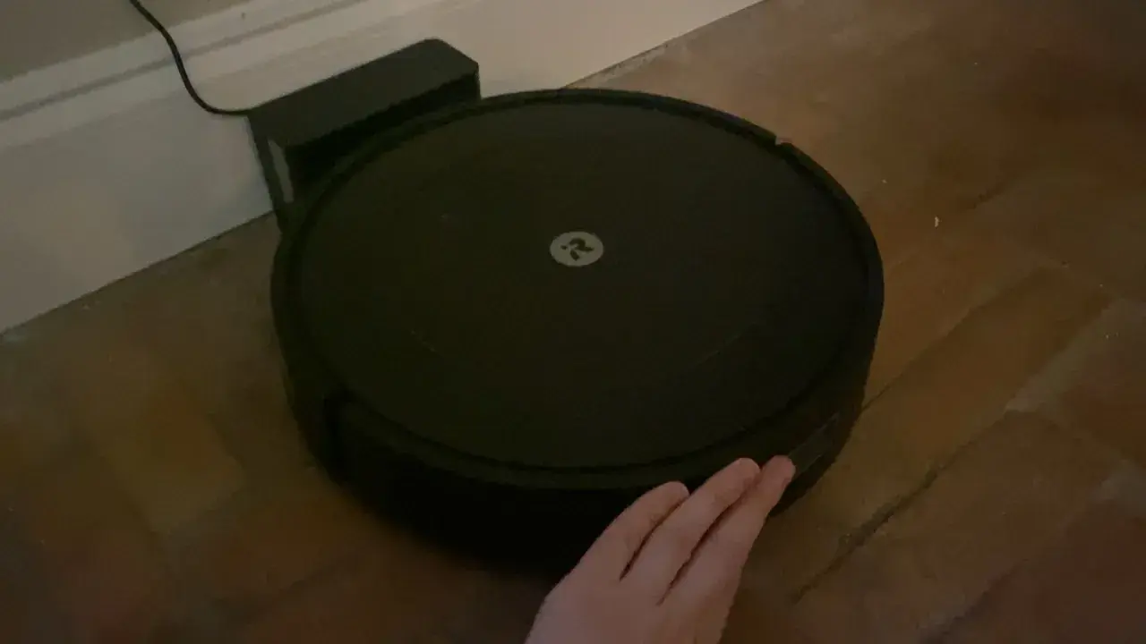 Robot aspirador Roomba con logo, conectado a su base. Una mano intenta interactuar, pero parece que hay un error 47.