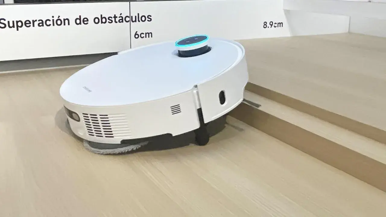 Robot aspirador blanco sobre suelo laminado, superando un pequeño desnivel.