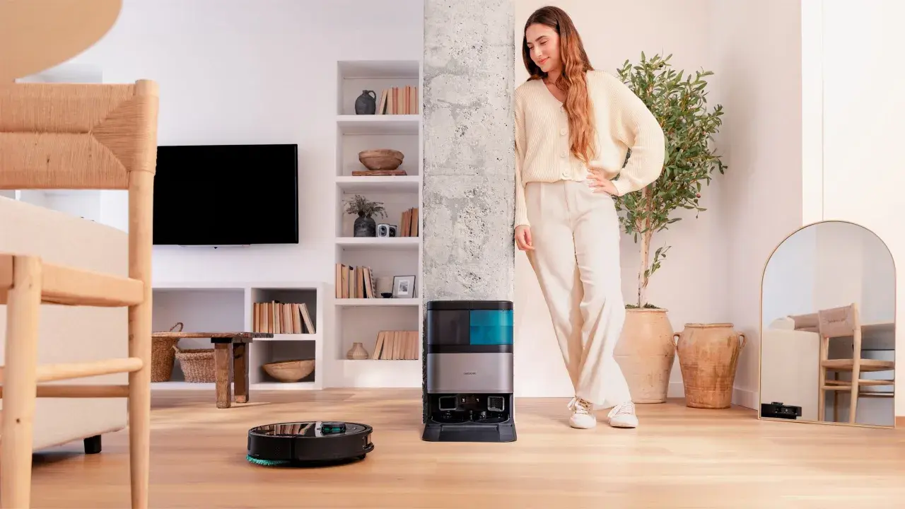 Una mujer sonríe junto a su nueva conga, un robot aspirador que limpia el suelo mientras ella descansa.