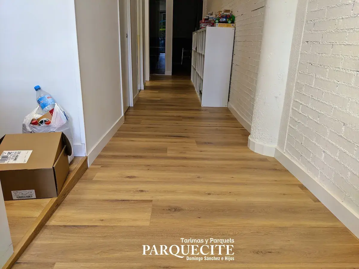 Pasillo con tarima de madera, ideal para saber como colocar tarima en pasillos. Se ven cajas y una botella de agua.