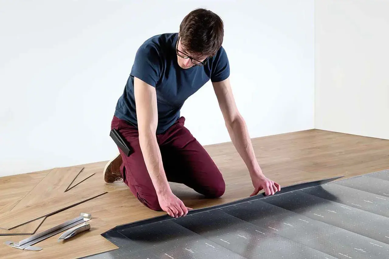 Hombre con gafas instalando suelo laminado sin experiencia. Herramientas y lamas de madera a su lado.