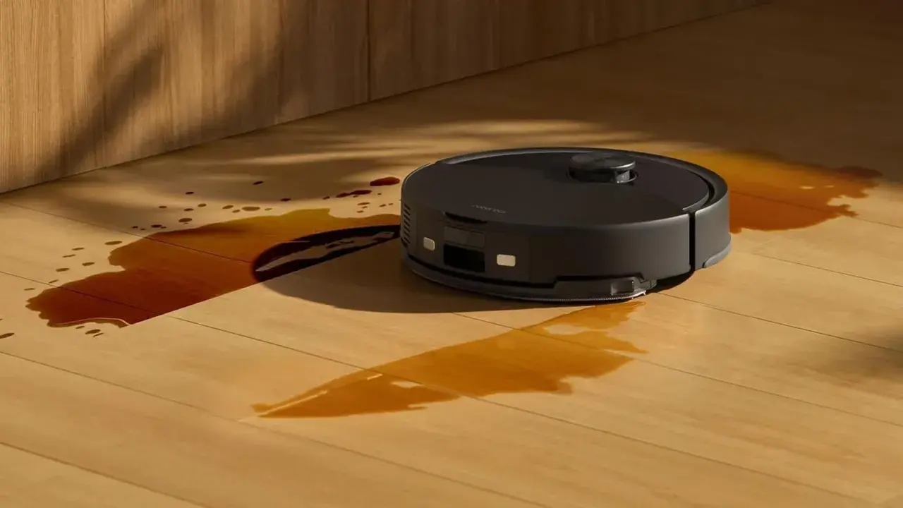Robot aspirador negro limpiando un derrame de líquido marrón en un suelo de madera. ¿Cuánto dura un robot aspirador?