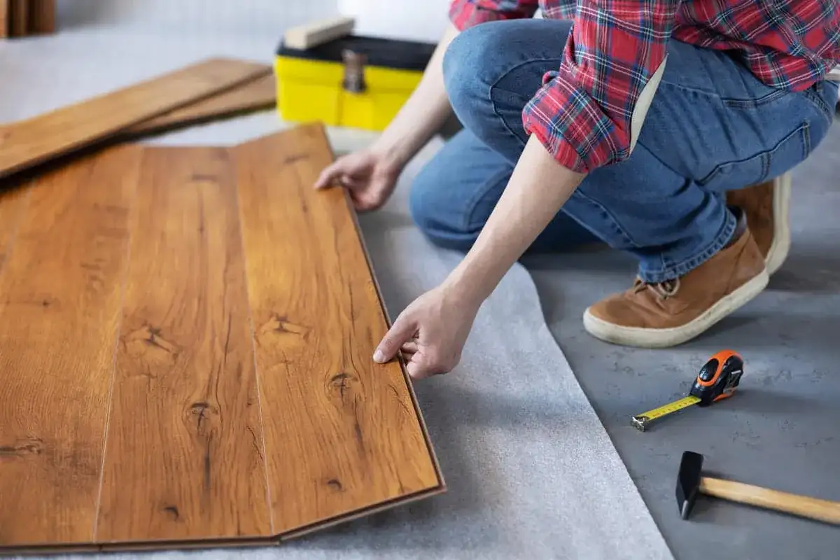 Persona instala parquet flotante de madera, colocando una tabla sobre otra.