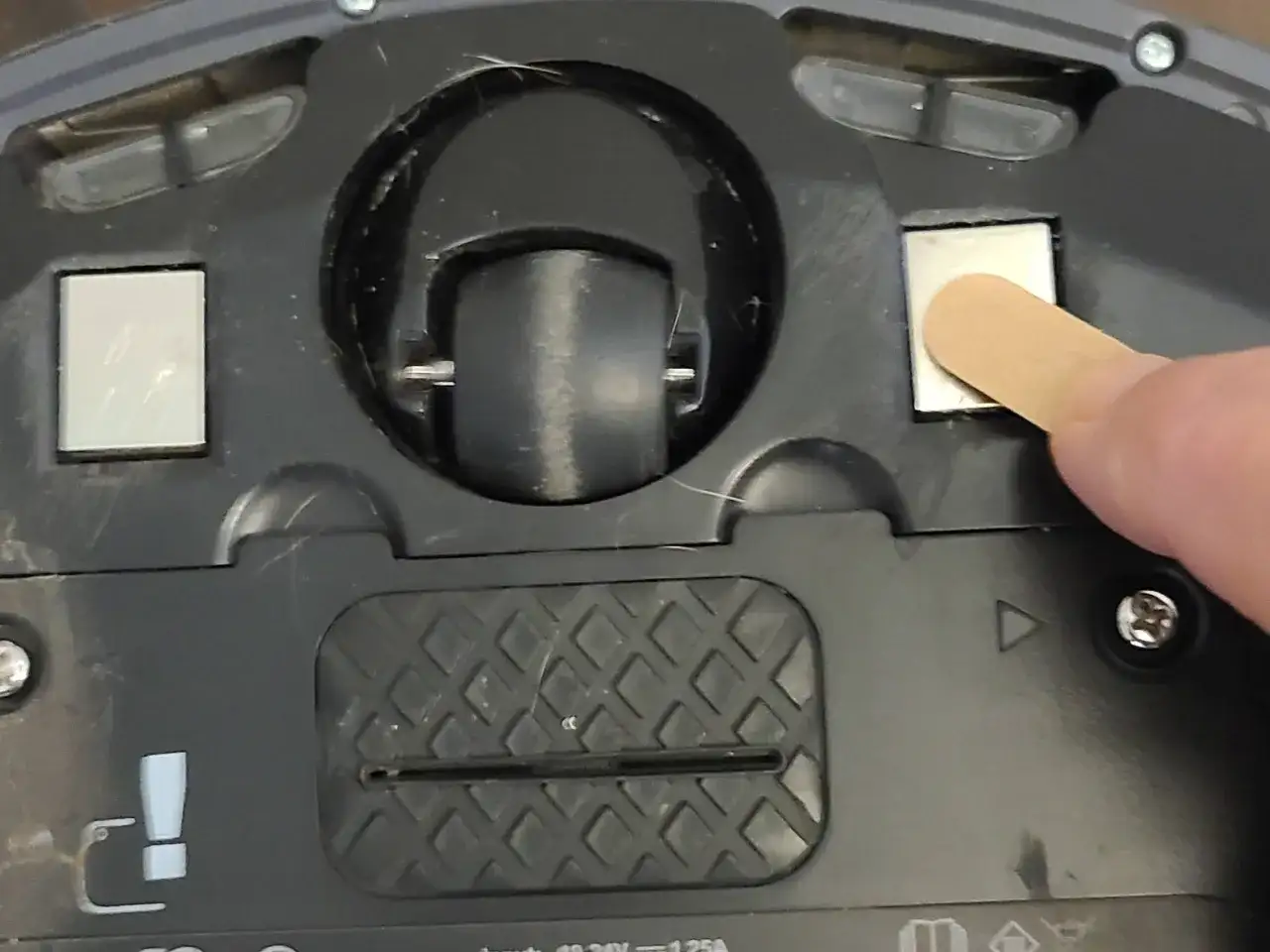 Un dedo usa un palillo para limpiar los contactos de carga de una Roomba que no carga en la base.
