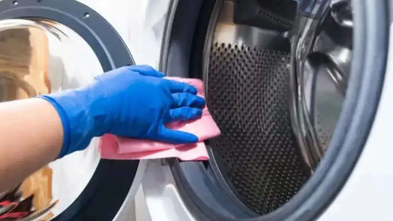Mano con guante azul limpiando el tambor de una lavadora con un paño rosa. Guía para saber como limpiar la lavadora.