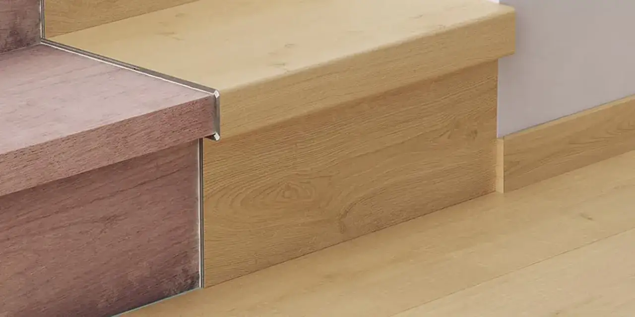 Detalle de escaleras con suelo laminado en tonos madera. Se aprecia el acabado de las huellas y contrahuellas, y el rodapié a juego.