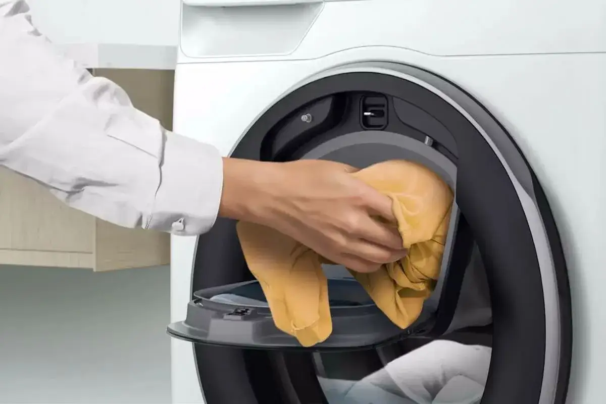 Mano colocando ropa amarilla en una lavadora moderna. &iquest;A qu&eacute; hora se puede poner la lavadora?