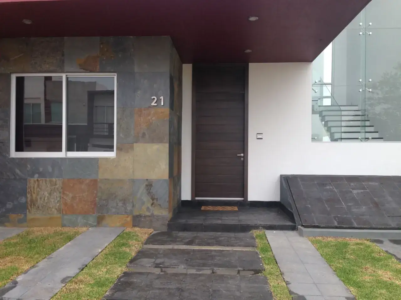 Modern entrance with slate tiles for suelos para entradas de casas, a dark wood door, and a glass staircase visible inside.