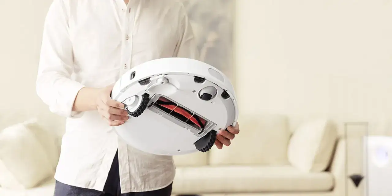 Persona sostiene un robot aspirador, mostrando su cepillo central para una limpieza eficiente.
