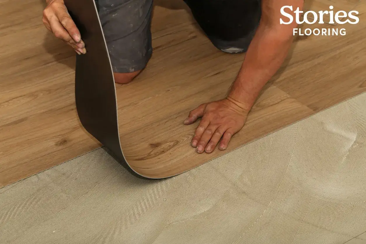 Instalación de suelo vinílico adhesivo o click. Manos colocando una lámina de vinilo imitación madera sobre base preparada.