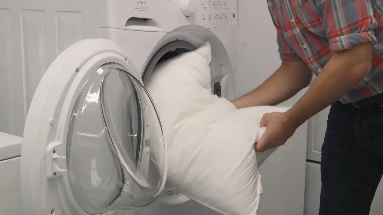 Hombre colocando almohadas blancas en lavadora para lavarlas.