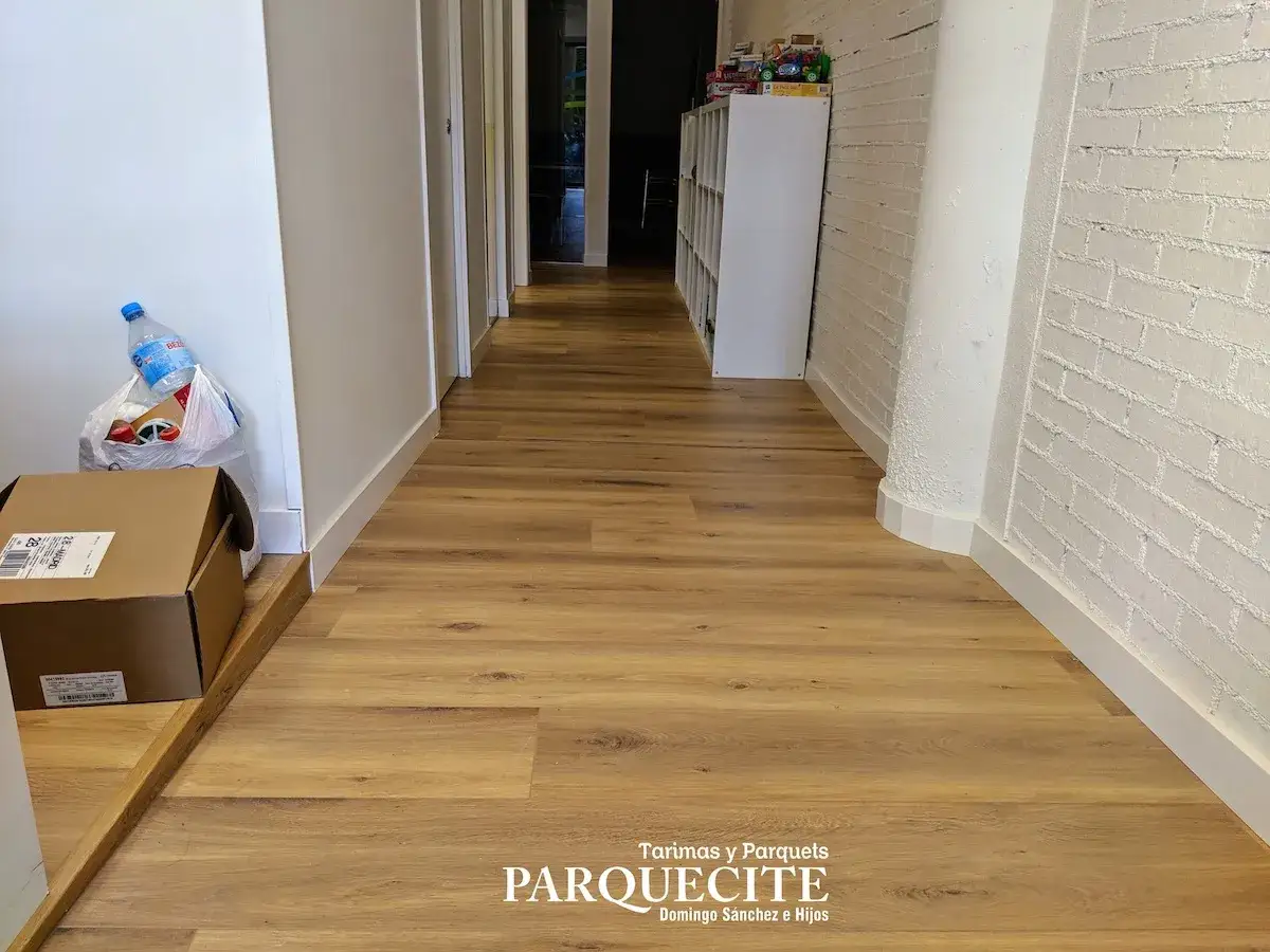 Pasillo con tarima de madera, ideal para saber como colocar tarima en pasillos. Se ven cajas y una botella de agua.