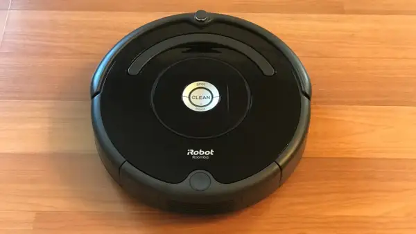 Un robot aspirador Roomba, uno de los modelos antiguos, descansa sobre un suelo de madera.