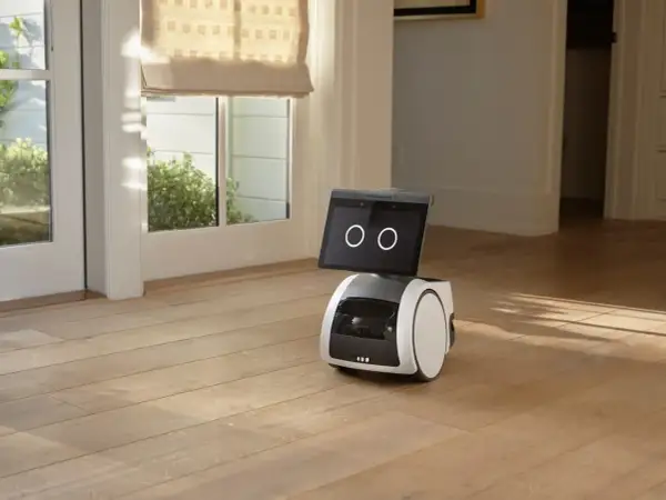 El robot Alexa Astro, con pantalla y ruedas, se encuentra en un suelo de madera, cerca de una puerta acristalada.