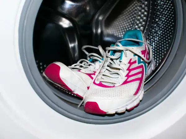 Un par de deportivas blancas con detalles fucsia y turquesa listas para lavar en lavadora.