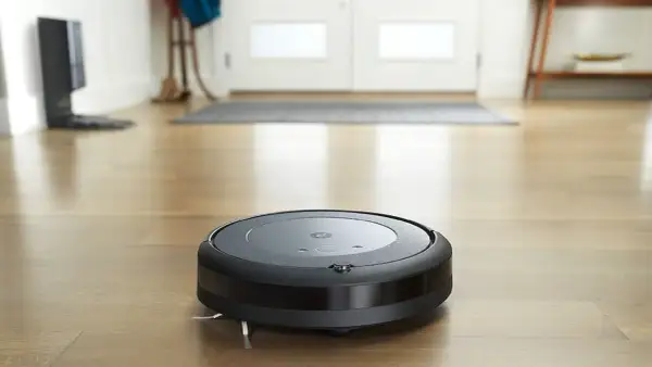 Un Roomba i3 negro aspira el suelo de madera.