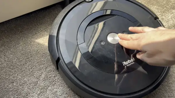 Mano presionando el botón "CLEAN" en un Roomba e5, quizás por **roomba e5 problemas**.