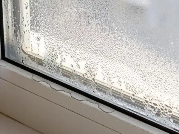 Gotas de agua cubren un cristal de ventana, mostrando cómo evitar condensación en ventanas. El agua se acumula en el alféizar.