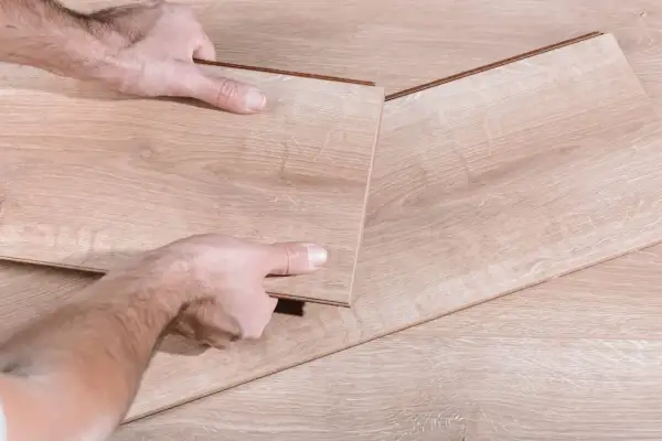 Manos desmontando una tabla de suelo laminado.