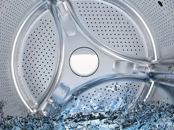 Interior de lavadora con agua salpicando. Averigua cuántos litros gasta una lavadora para optimizar tu consumo.