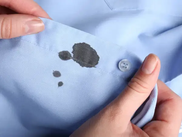 Manos sostienen una camisa azul con manchas de tinta. Aprende como quitar las manchas de tinta de la ropa.