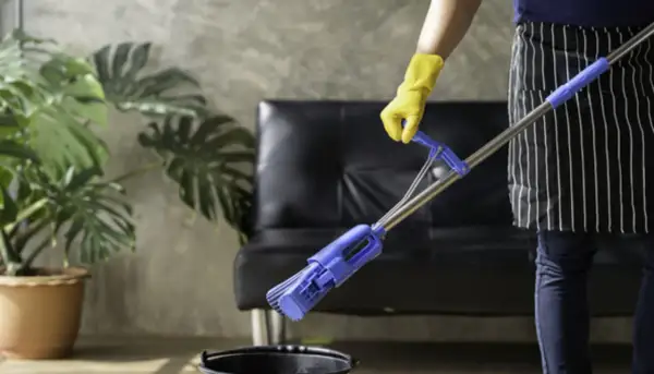 Persona con guantes amarillos y delantal a rayas friega el suelo con una mopa azul.
