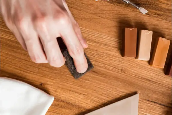 Mano lijando para reparar suelo laminado. Cera de colores y espátula listas para el retoque.