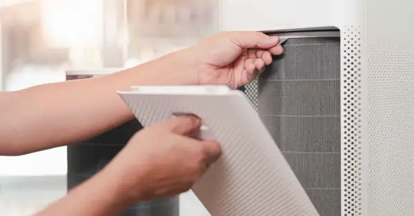 Persona saca un filtro HEPA de un purificador de aire para limpiarlo.