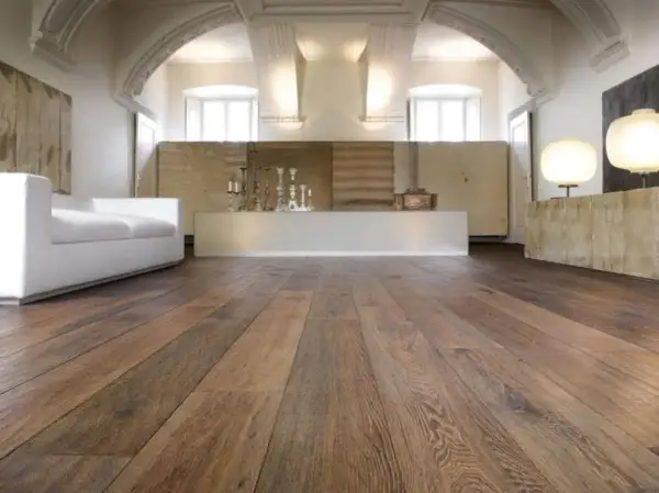 Acuchillado de parquet de madera rústica en un salón moderno con sofá blanco y lámparas.