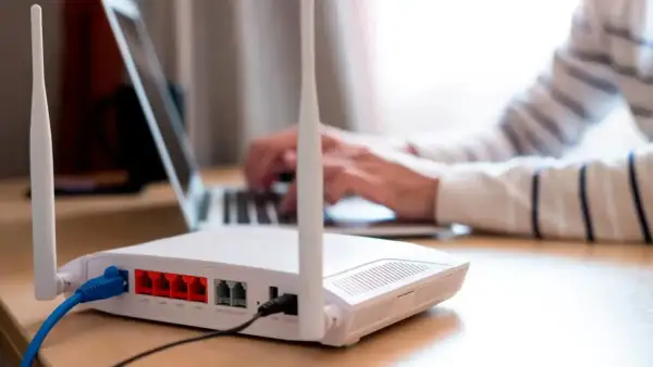 Persona frustrada intenta conectar un portátil a un router que no se enciende. Cables azules y negros conectados.