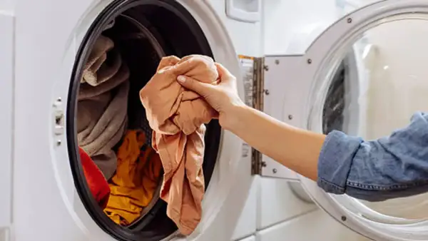 Mano saca ropa de lavadora. Un truco para limpiar lavadora con vinagre es añadirlo al ciclo de lavado.