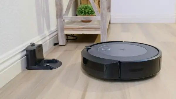 Aspiradora robot negra junto a su base de carga, lista para un mapeo rápido del hogar.