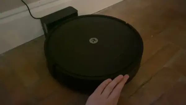 Robot aspirador Roomba con logo, conectado a su base. Una mano intenta interactuar, pero parece que hay un error 47.