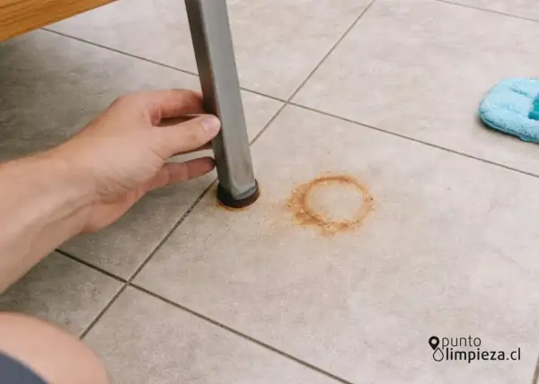 Mano levantando pata de mueble para mostrar cómo quitar manchas de óxido en el suelo de baldosas.