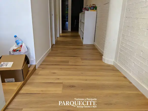 Pasillo con tarima de madera, ideal para saber como colocar tarima en pasillos. Se ven cajas y una botella de agua.