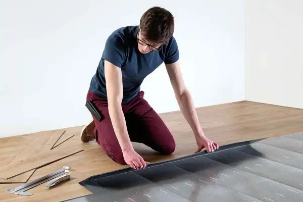 Hombre con gafas instalando suelo laminado sin experiencia. Herramientas y lamas de madera a su lado.
