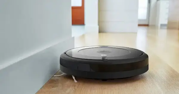 Robot aspirador Roomba negro junto a una pared blanca, listo para resetear y limpiar el suelo de madera.