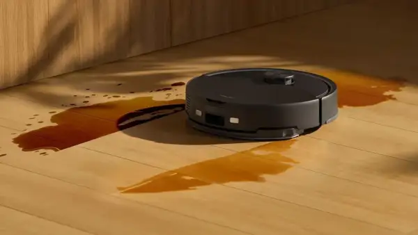 Robot aspirador negro limpiando un derrame de líquido marrón en un suelo de madera. ¿Cuánto dura un robot aspirador?
